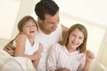 Man with two young children sitting in bed smiling