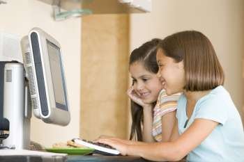 Two young girls in kitchen with computer smiling