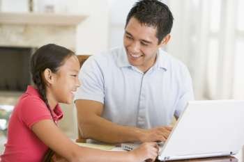 Man and young girl with laptop in dining room smiling