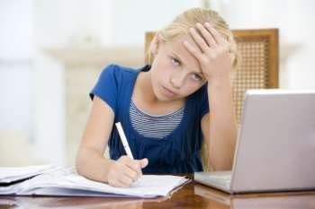 Young girl with laptop doing homework in dining room looking unhappy
