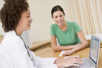 Doctor using laptop with woman in doctor´s office smiling