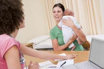 Doctor with laptop and woman in doctor´s office holding baby