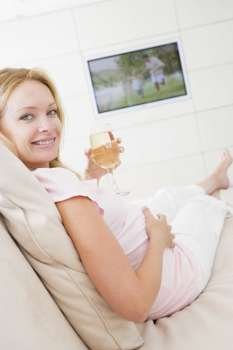 Pregnant woman watching television with glass of white wine smiling