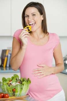 Pregnant woman in kitchen making a salad and smiling