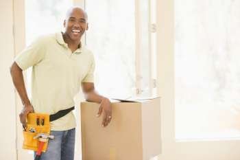 Man wearing tool belt standing by boxes in new home smiling