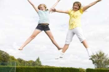 Two young girls jumping on trampoline smiling