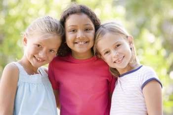 Three young girl friends standing outdoors smiling