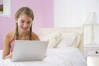 Teenage Girl Lying On Bed Using Laptop 