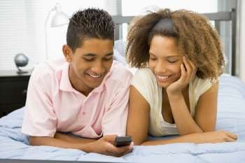 Teenagers Lying On Bed Together Looking At Mobile Phone