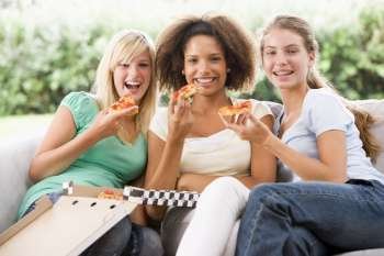 Teenage Girls Sitting On Couch And Eating Pizza Together