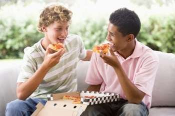 Teenage Boys Sitting On Couch Eating Pizza Together