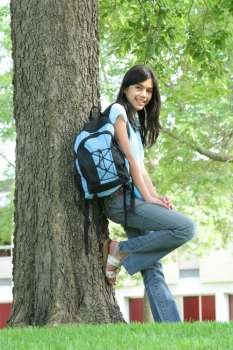 Young teen girl standing with backpack by tree, smiling. Part asian, Scandinavian descent.