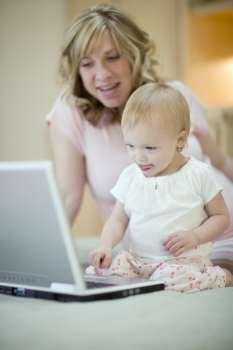 Pregnant woman teaching baby daughter to use laptop