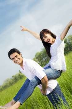 Man giving woman piggyback in meadow, laughing. Narrow focus on his eye. 