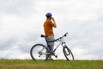 Man with mountain bike in a meadow talking on mobilel phone 