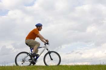 Man riding a mountain bike in a meadow against cloudy sky 