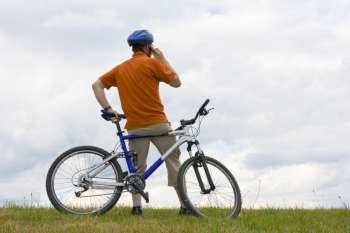 Man with mountain bike on a meadow talking on cell phone 