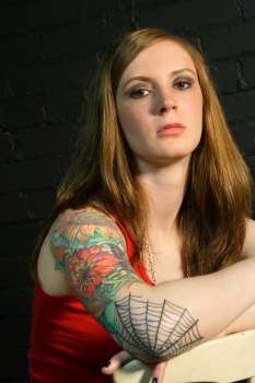 A young female with serious stare and arm tattoo. 