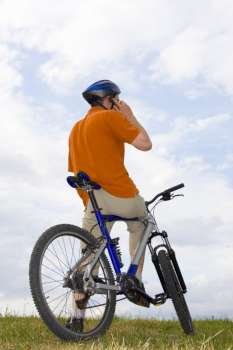 Man with mountain bike on a meadow making a phone call 