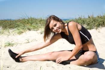 A beautiful caucasian girl stretching on the beach before exercising