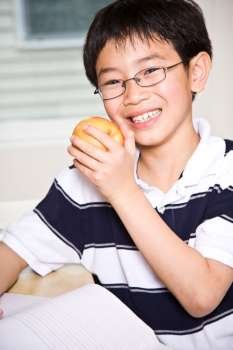 A shot of an asian kid studying and eating an apple at home