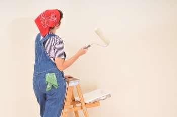Woman in overalls standing on ladder with paint roller 