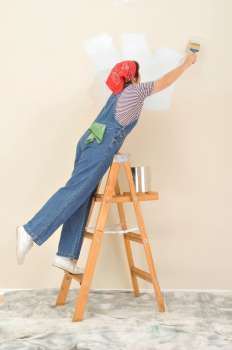 Woman standing on ladder stretching to paint wall 