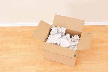 Open cardboard moving box with packing paper in empty room 