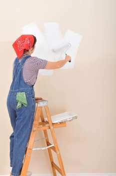Woman on ladder using roller to paint the interior of her house 
