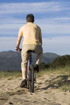 Man riding bicycle on the beach with hills in the background 