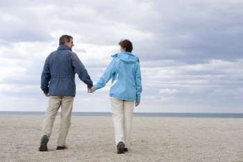 Mid-adult couple walking hand in hand on the beach 