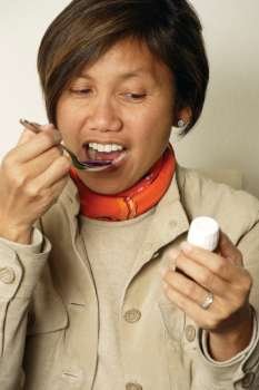 An Asian female in her early 40´s taking a spoonful of cough medicine. 