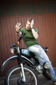 Portrait of young man sitting on motorbike and looking at mirror 