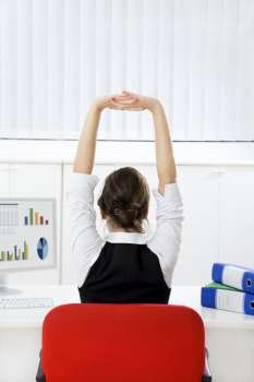Rear view of young businesswoman sitting at desk stretching. Copy space 