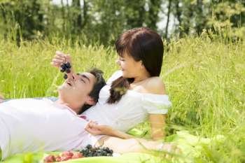 Couple lying in grass, smiling and eating grapes 