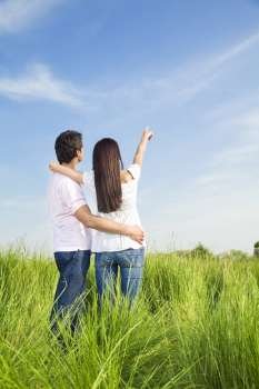 young couple in meadow with hand in air, hugging and smiling. Copy space 