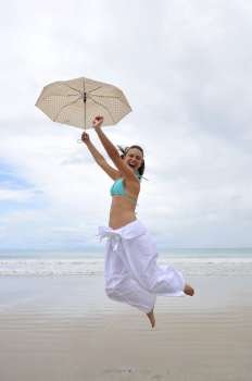 woman jumping on a tropical beach holding an umbrella 