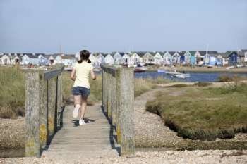young girl running over foot bridge away from camera with beach huts in backgrounds