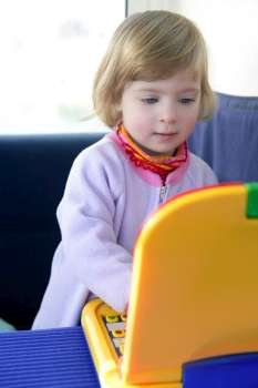 Beautiful toddler little girl thinking playing with yellow laptop toy computer