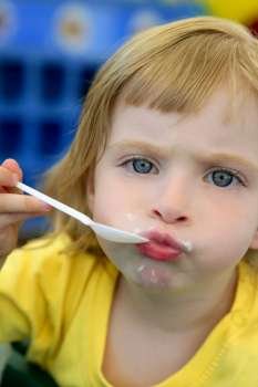 Adorable blond little girl eating and gesturing with spoon