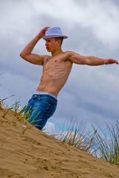 Barechested young man stands with hand on head on a sand dune