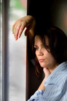 Mid-adult woman in man's shirt leans on window frame
