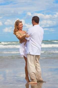 A young man and woman having fun laughing and embracing as a romantic couple on a beach with a bright blue sky