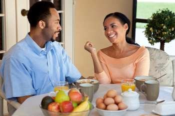 A happy African American man and woman couple in their thirties sitting outside having a healthy breakfast