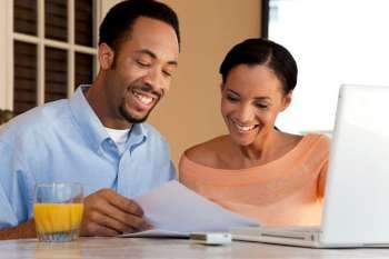 A happy African American man and woman couple in their thirties working on a laptop computer and looking at paperwork
