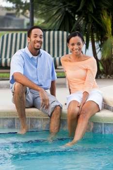 A happy African American man and woman couple in their thirties sitting wth their feet in a swimming pool