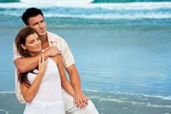 A young man and woman embracing as a romantic couple on a beach