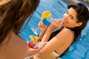 A beautiful young Hispanic woman sitting by a swimming pool and enjoying a cocktail with her friends