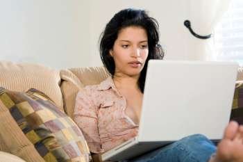 A stunningly beautiful young Hispanic woman sitting on a settee using her laptop