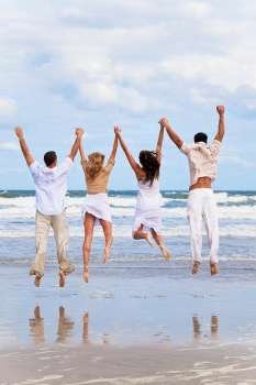 Four young people, two couples, holding hands, having fun and jumping in celebration on a beach